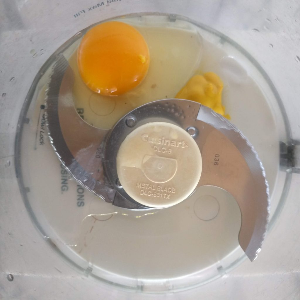Food processor bowl with mayonnaise ingredients before blending.