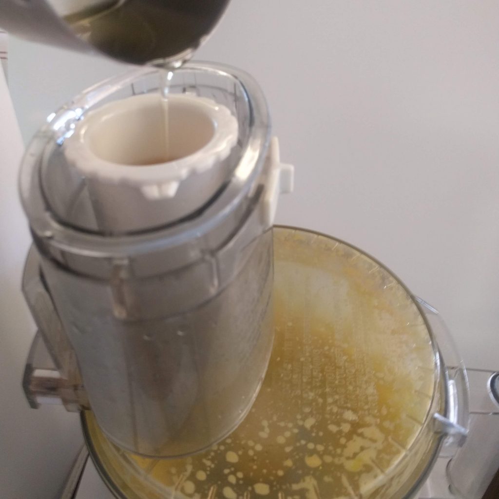 Pouring the oil into the pusher with food processor on.