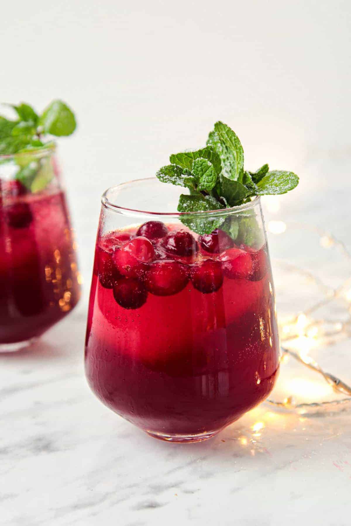 cranberry pomegranet spritzer with peppermint leaf in a cocktail glass, with  Christmas light