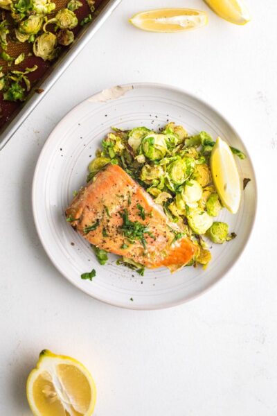 cooked salmon with brussel sprouts and herbs served topped with herbs with a slice of lemon on a white plate