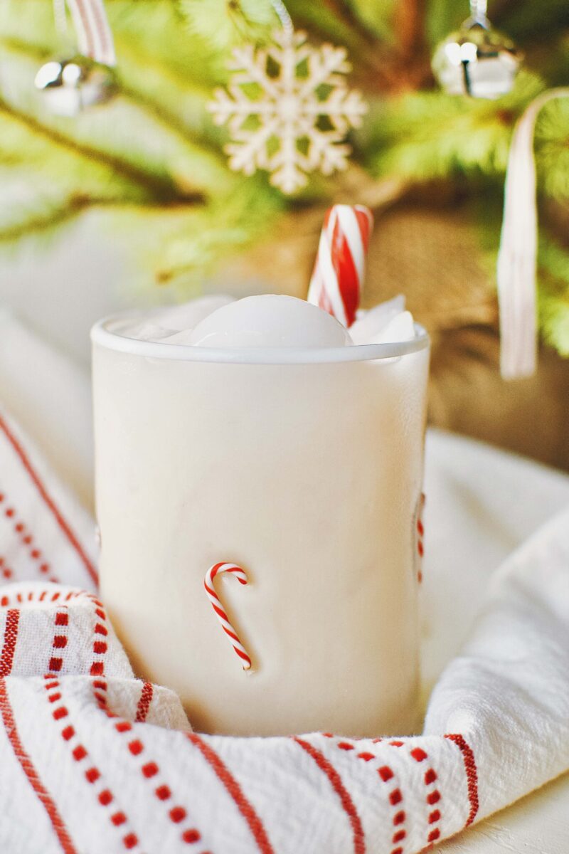 Eggnog coktail with candy canes in a candy cane decorated transparent glass