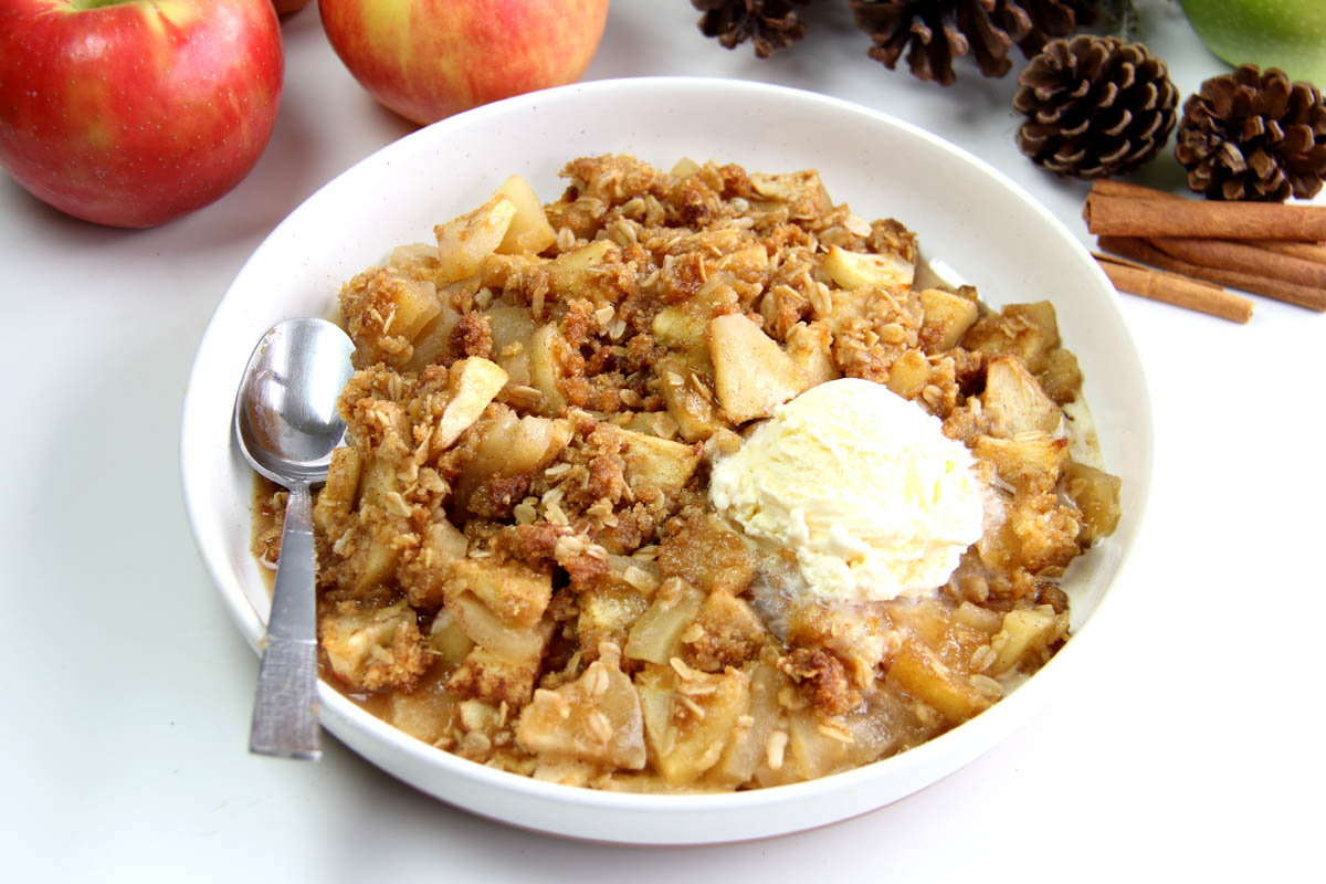 gluten free apple oatmeal crisp topped with ice cream with spoon on a white bowl plate