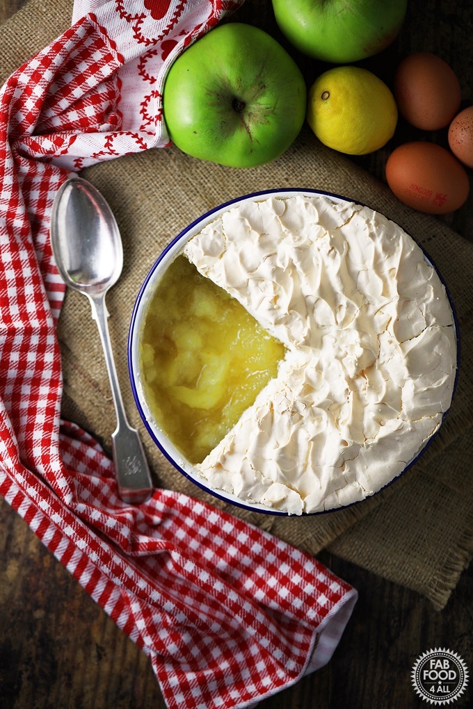 apple meringue with soft pillowy sits aloft a bed of stewed apples, with spoon, and checkered red tablecloth