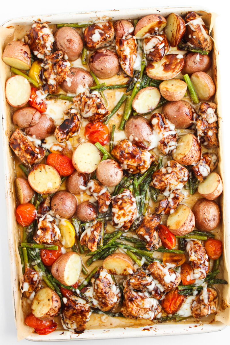 Balsamic chicken and veggies on sheet pan on white background.