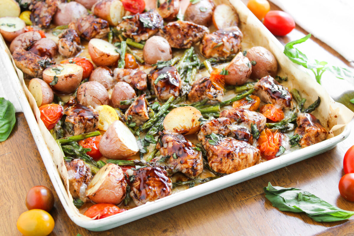 Edge of sheet pan with Balsamic chicken and veggies on a wood table.