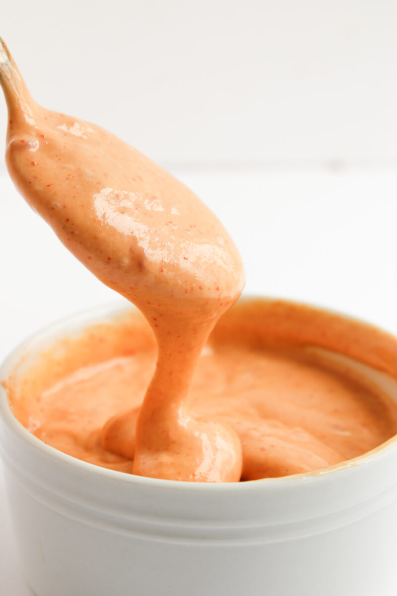 Bang bang sauce dripping off a spoon into a white bowl