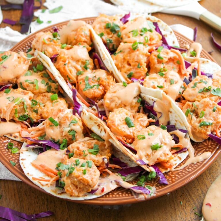6 bang bang shrimp tacos in a row on a large brown plate