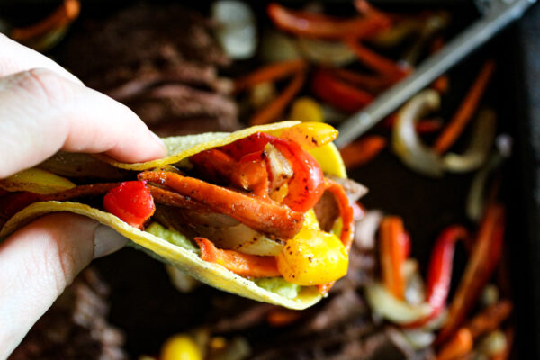 hand holding a fajita in tortilla over sheet pan