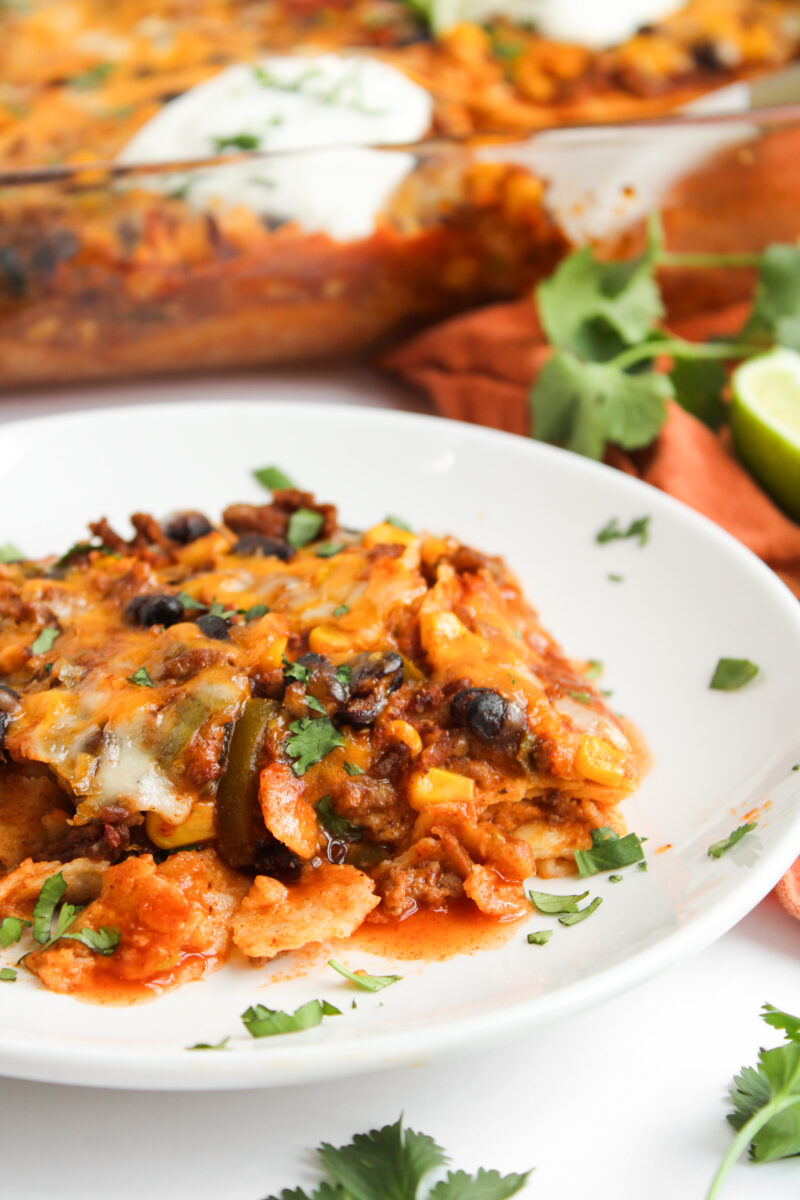 Serving of beef enchilada casserole on a white plate with cilantro sprinkled around it.