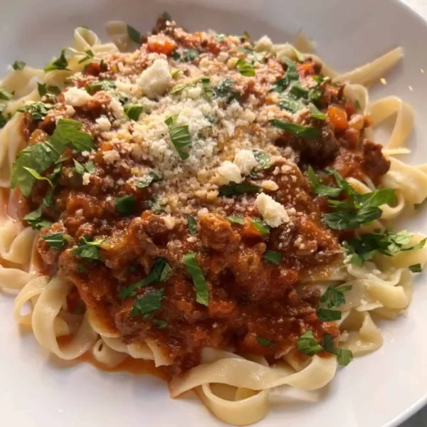 cooked pasta with tomato sauce, meat, herbs and parmesan cheese in a white plate