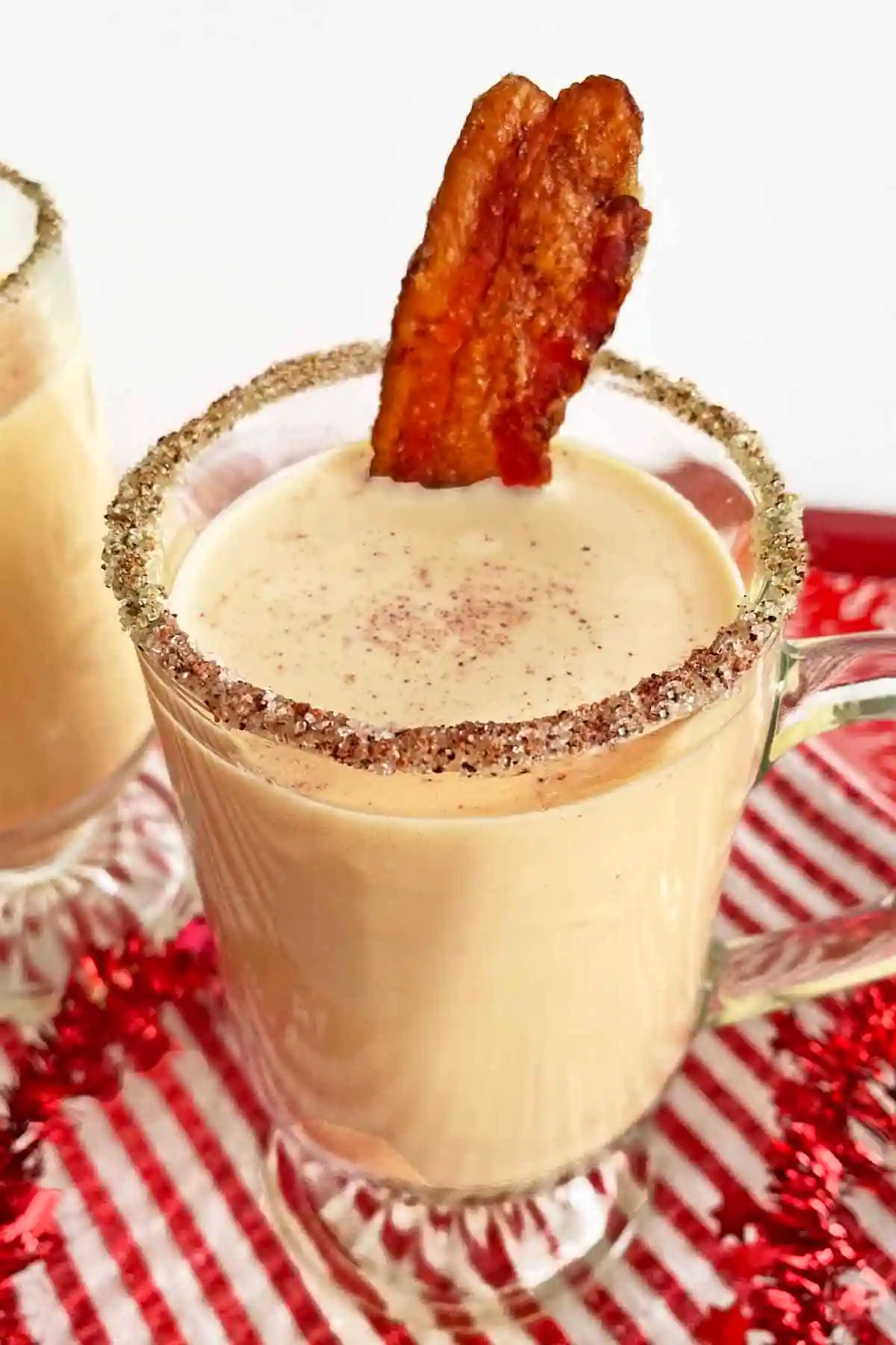 festive Praline Bourbon Eggnog rimmed with sugar with a strip Candied Maple Bacon 