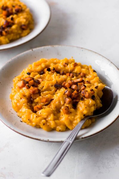 butternut squash risotto topped with pepper powder on a white plate with a spoon