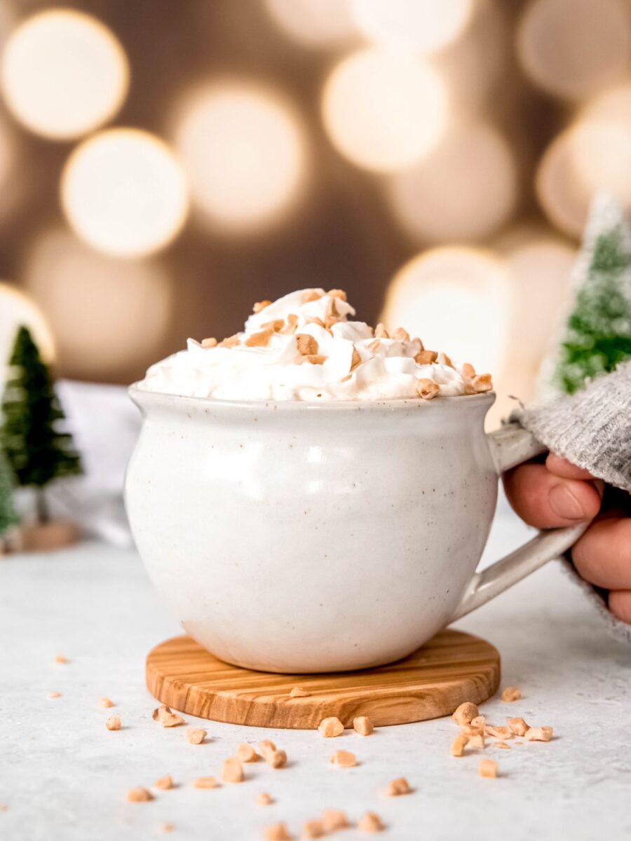 caramel brulee latte with whipped cream topped with toffee bits in a white mug