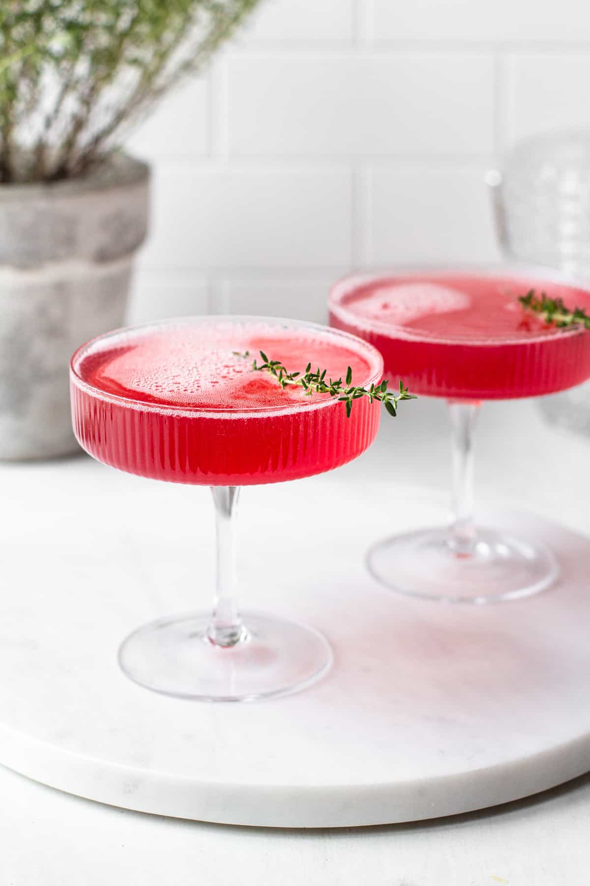 champagne cocktail with elderflower syrup garnished with sprig of thyme in champagne coupes