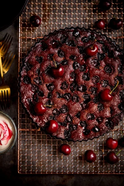 baked gluten-free chocolate black forest cherry cake topped with fresh cherries on a wire baking rack