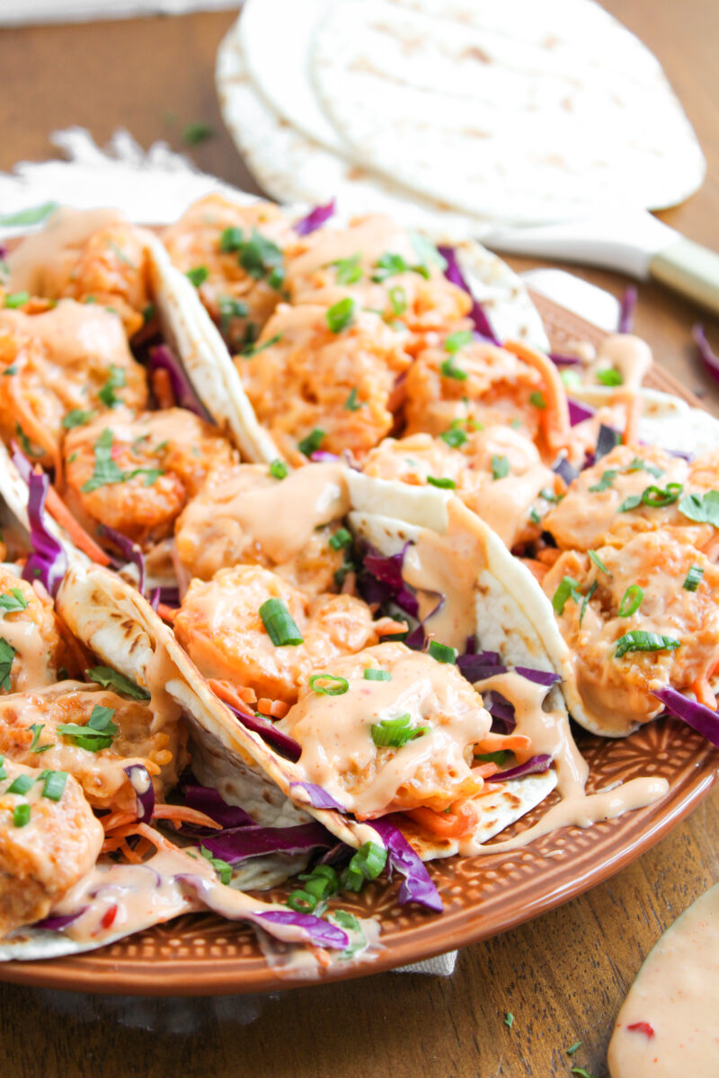 Close up of one bang bang shrimp taco in a row on a large brown plate.