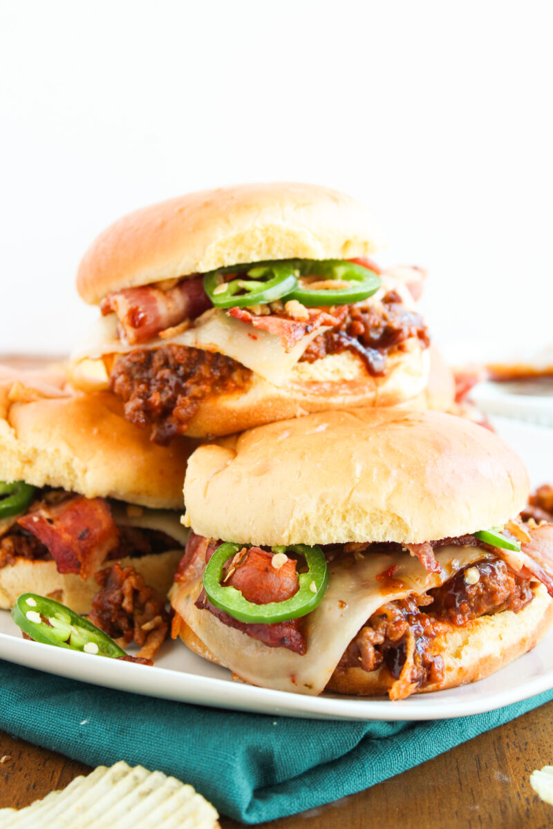 Three sloppy joes in a pile on a white plate with a green napkin underneath.