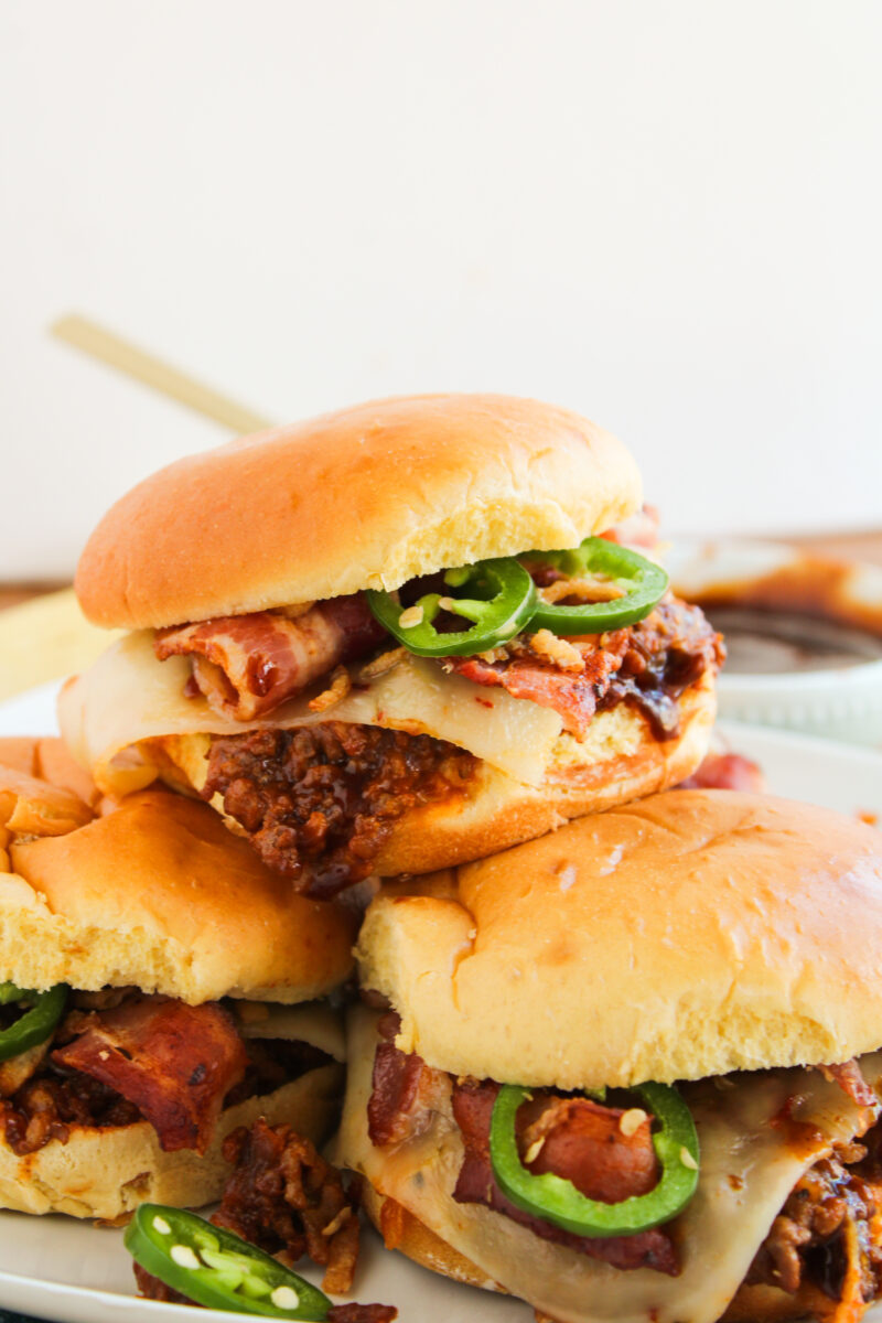 Close up of sloppy joe on top in a pile on a white plate with bowl of BBQ sauce in the background.