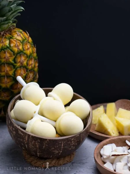 mini pineapple and coconut popsicle in a coconut bowl with a whole pineapple fruit and  pineapple slices on the side