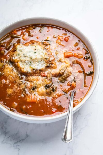 cooked beans and elbow pasta are in a rich tomato broth with parmesan dumplings in a white bowl on a marble white table
