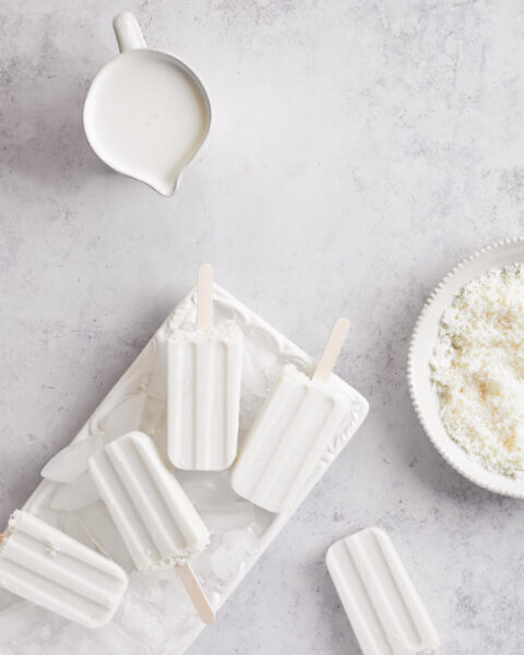 white dairy free coconut popsiles served with ice cubes on a rectangular plate laid on a white marrble countertop