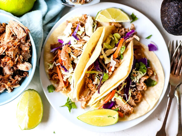 crockpot pulled pork tacos on a white plate with lime 
