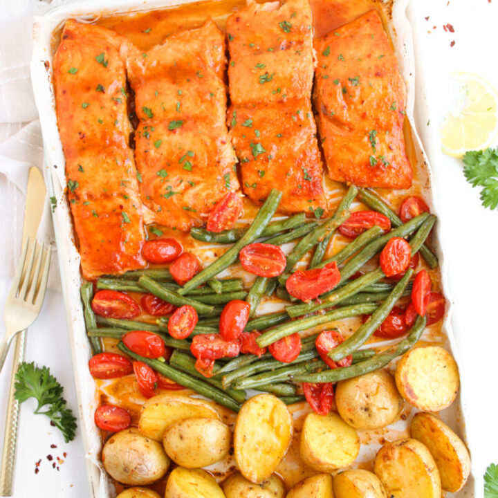 Flat lay of salmon, vegetables, and potatoes on baking sheet with gold fork, napkin, and ingredients around it.