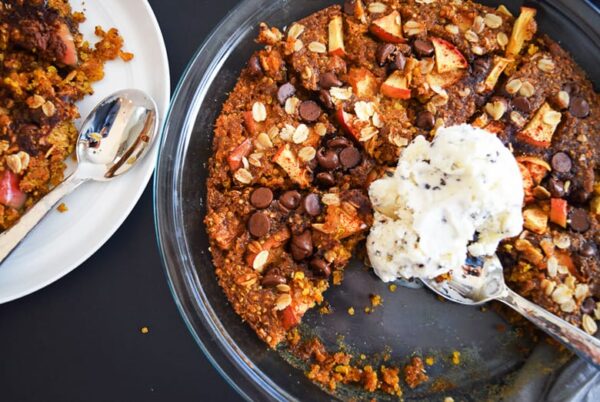 baked Apple Crisp with quinoa, oats and almond flour topped with chocolate chips and icre cream on a round glass baking dish with a spoon