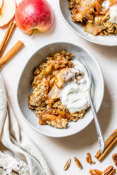 baked gluten-free apple crisp with caramelized apples, oats, and almond flour topped with ice cream in a white bowl with a spoon