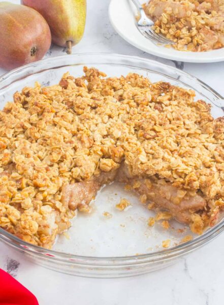baked gluten-free pear crisp with oats on a round glass baking dish with pears in the background