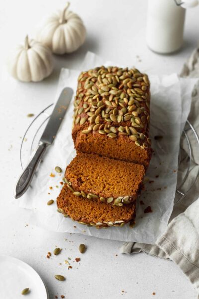 baked gluten free pumpkin bread loaf topped with pumpkin seeds with bread knife on the side
