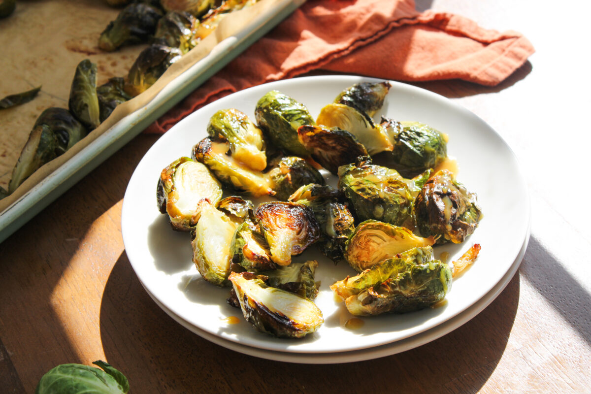 Brussels sprouts on stacked white plates with sheet pan and orange napkin in the background.