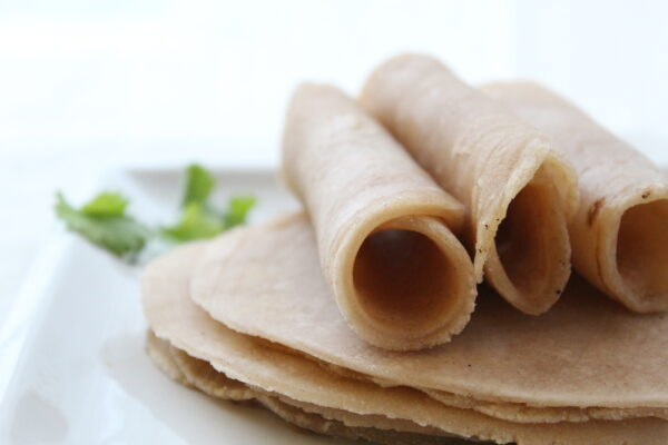 three rolled up tortillas on a white plate on a stack of more tortillas