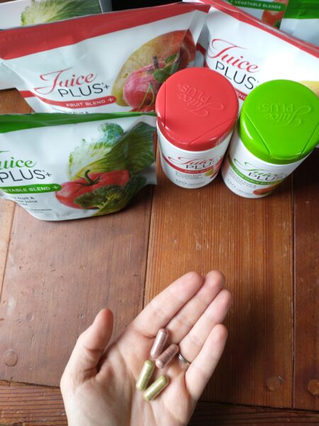 Juice Plus capsules in hand, with packages on table