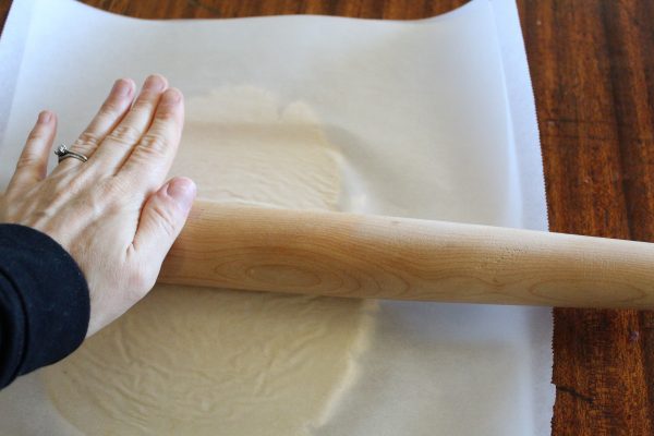 coconut flour pizza dough rolled out between two pieces of parchment