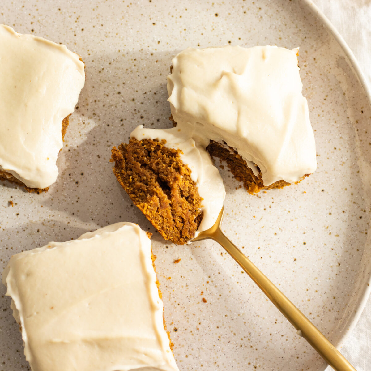 vegan pumpkin cake with cream cheese frosting sliced in squares with a spoon