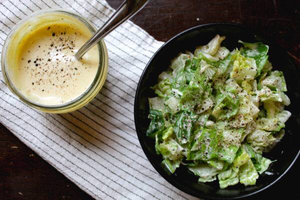 caesar dressing in jar next to black bowl with salad