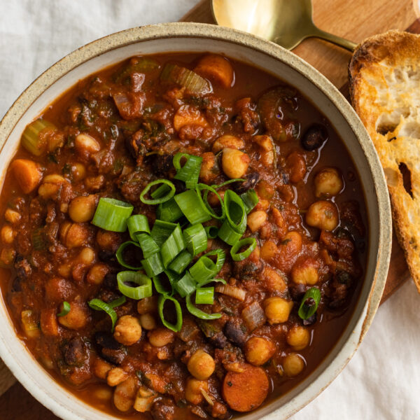 stew with beans and veggies topped with sliced spring onionsin a white-cream bowl