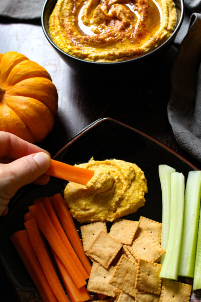 dipping carrot in pumpkin hummus on plate