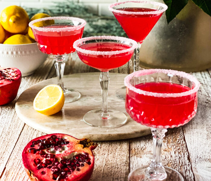 pomegranate lemon martini rimmed with white sugar in small glasses with slices of pomegranate and lemon