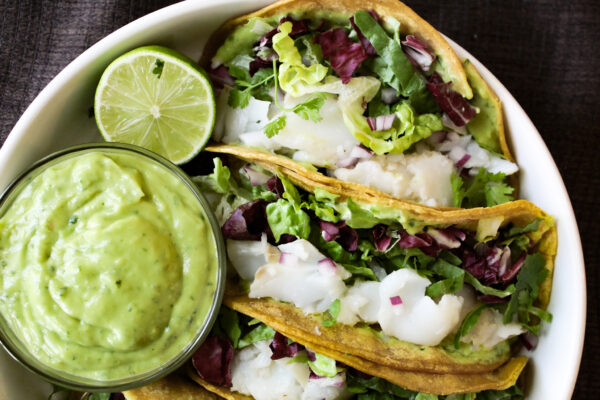 avocado lime dressing with fish tacos on white plate