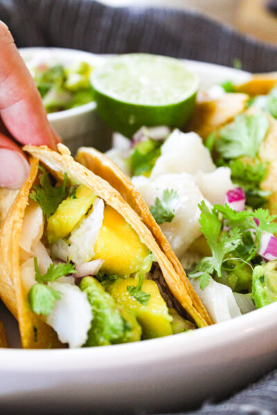 hand holding one fish taco with avocado mango salad