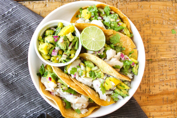 fish tacos with avocado mango salsa, in white plate on table