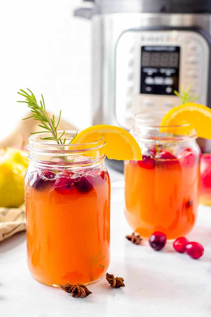 apple pear cider with cranberries, orange slices, and rosemary in glass mug jars