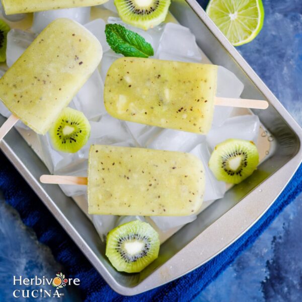 kiwi coconut popsile served on an oven dish with ice cubes, slices of kiwi and a sinle basil leaf