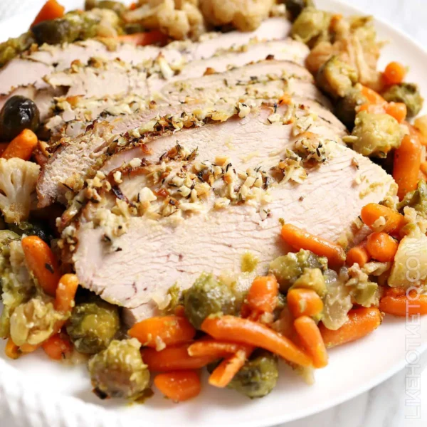 cooked slices of turkey breast topped with minced garlic and sorrouned by fall veggies on a white plate
