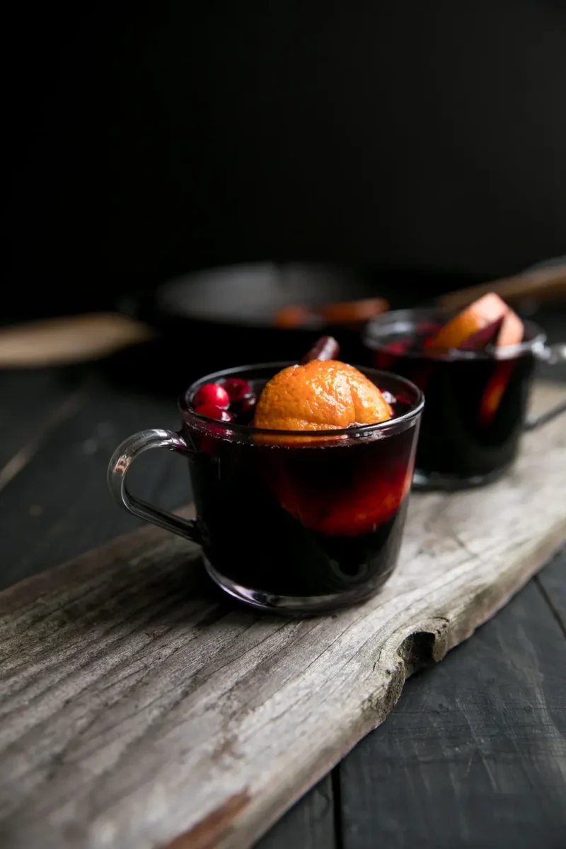 mulled red wine with blackberries, orange and cinnamon barks in small glasses with handles on wood