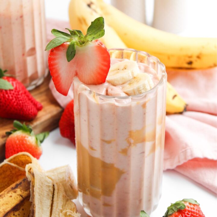 PB&J Smoothie in a glass cup with ingredients and pink napkin in the background.