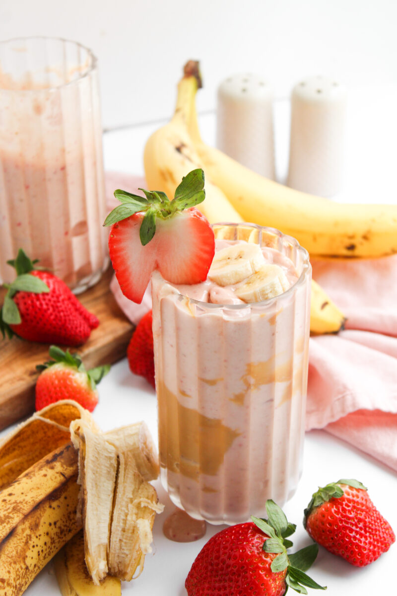 PB&J Smoothie in a glass cup with wood board, strawberries, and a second glass in the background.