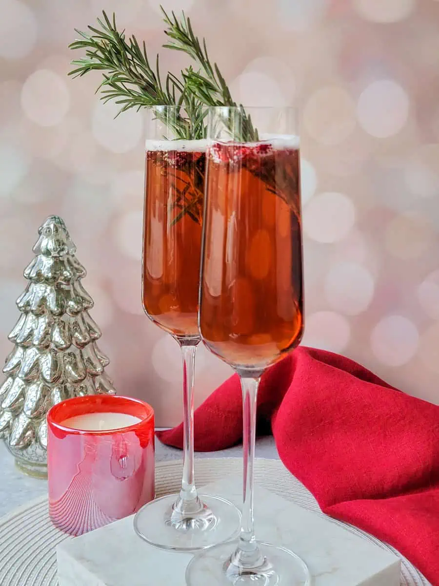 pomegranate mimosa with sprigs of rosemary in champagne flute glass, with festive decorations